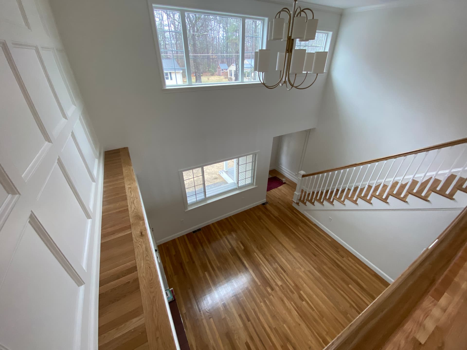 Finished two-story stair hall with hardwood floors, white millwork and a modern chandelier