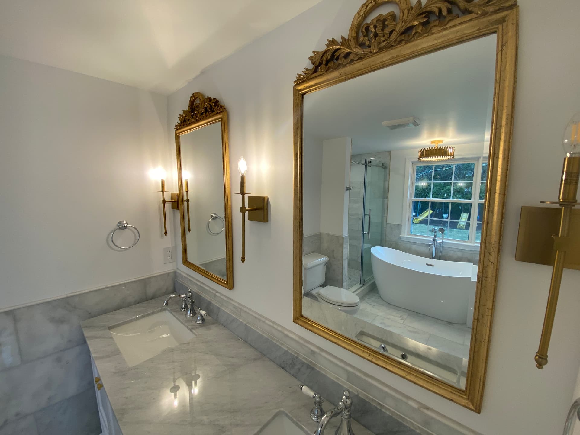 Primary bathroom marble vanity with gilded mirrors and brass sconces