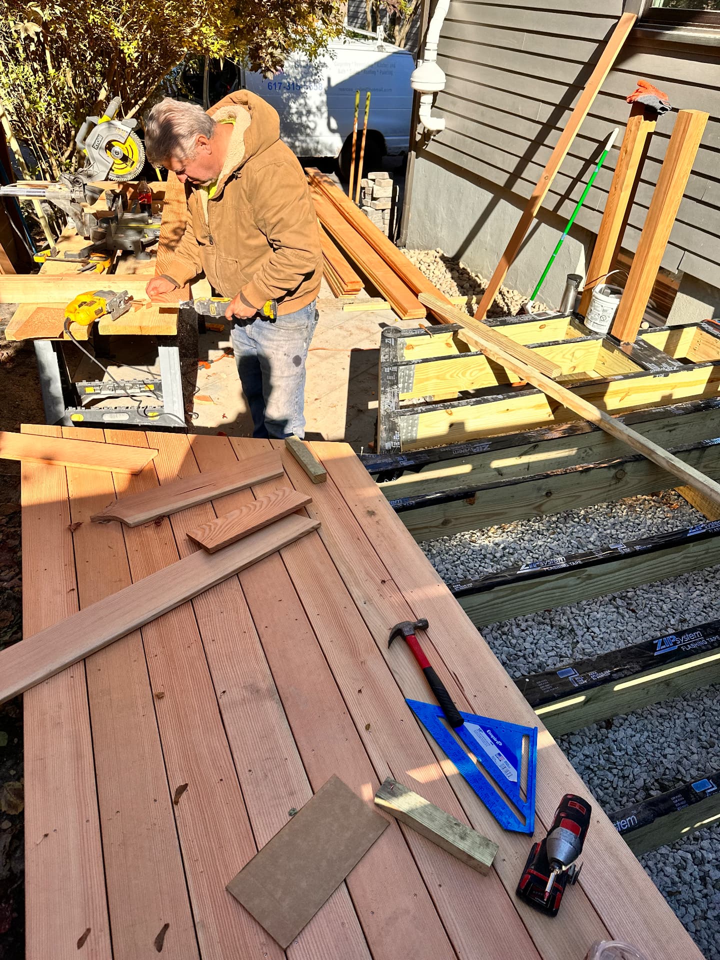 Carpenter cutting cedar decking beside the framed deck platform