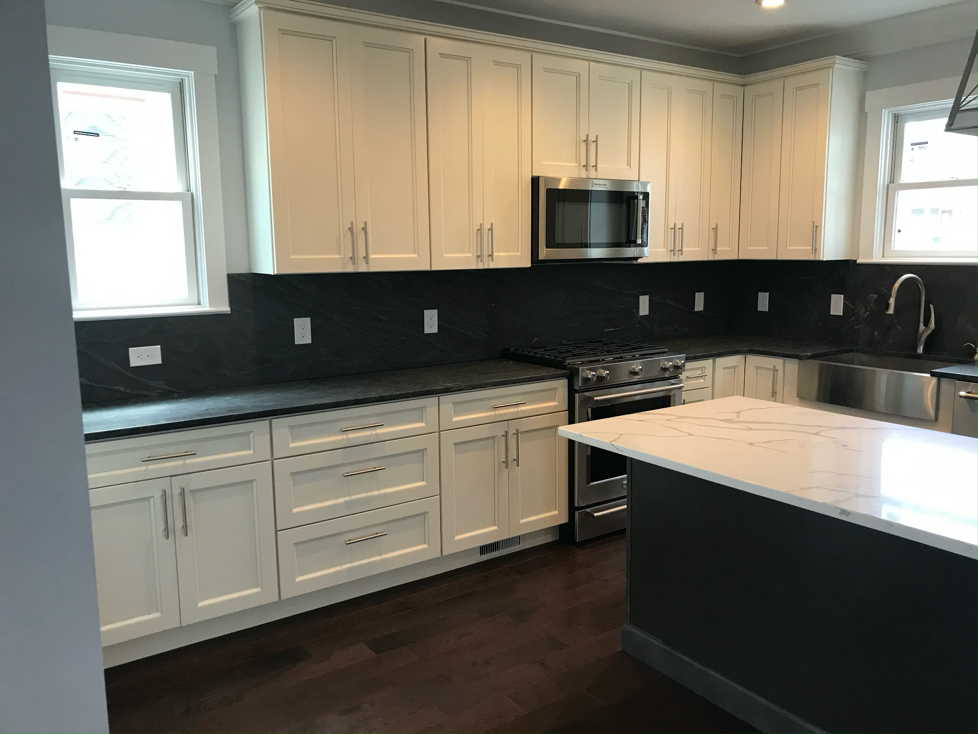 Renovated kitchen with white cabinetry and black stone backsplash